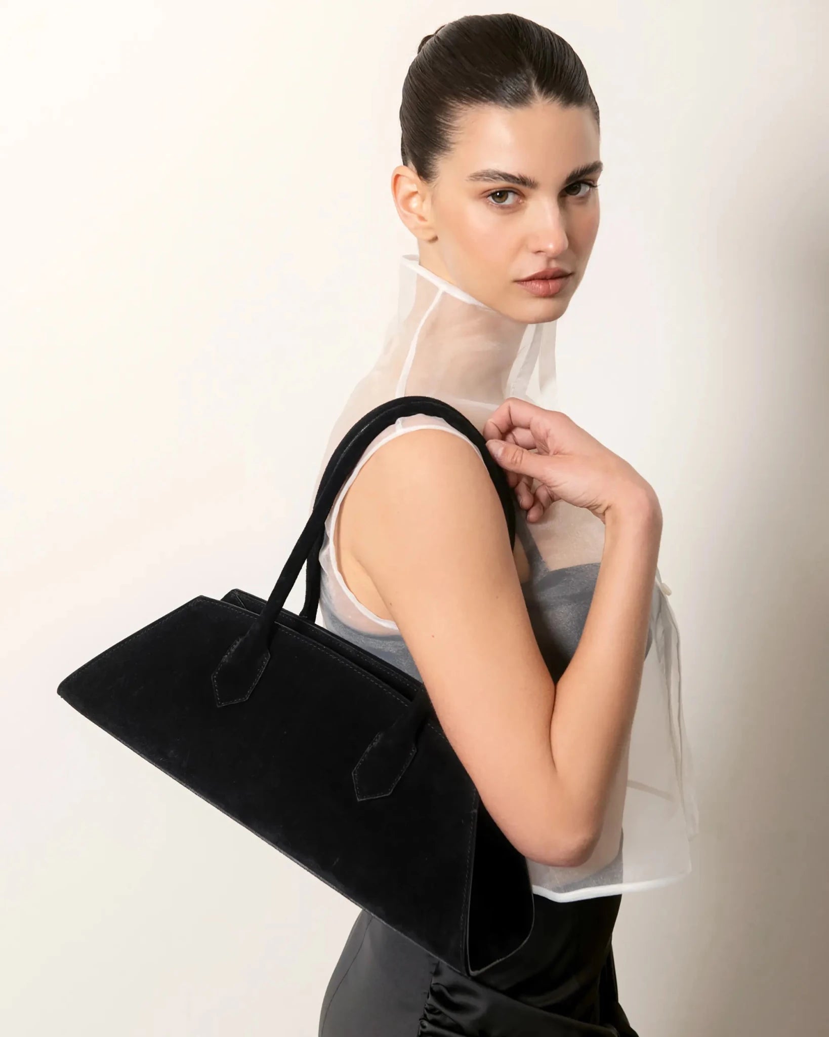 Modella con Bellucci MADBAG in suede nero, camicia bianca e gonna nera vista laterale